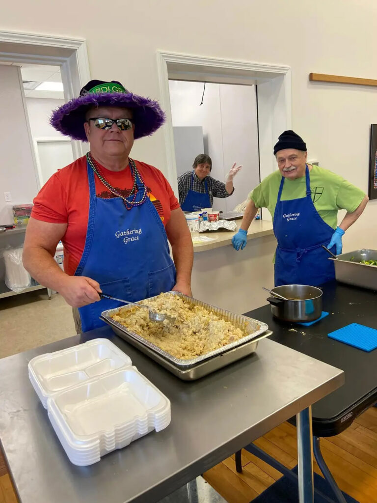 Three Gathering Grace Volunteers in Aprons Serving Food at Gathering Grace